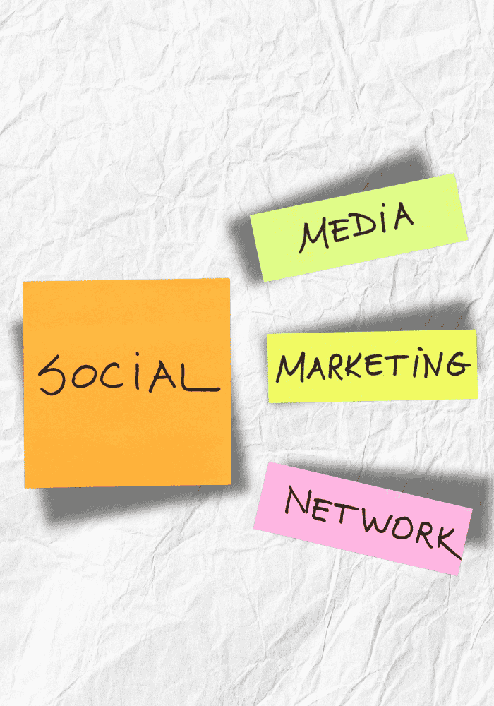 Four sticky notes on a crumpled white background. The notes are colored orange, yellow, and pink, and they contain the following handwritten text: "SOCIAL," "MEDIA," "MARKETING," and "NETWORK."